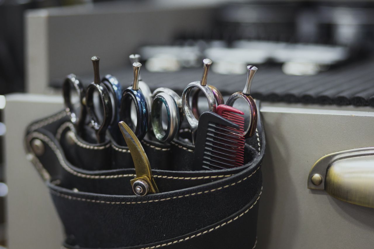 Strona Główna Close-up of barber tools in a leather holster, including scissors and combs, in a salon setting.