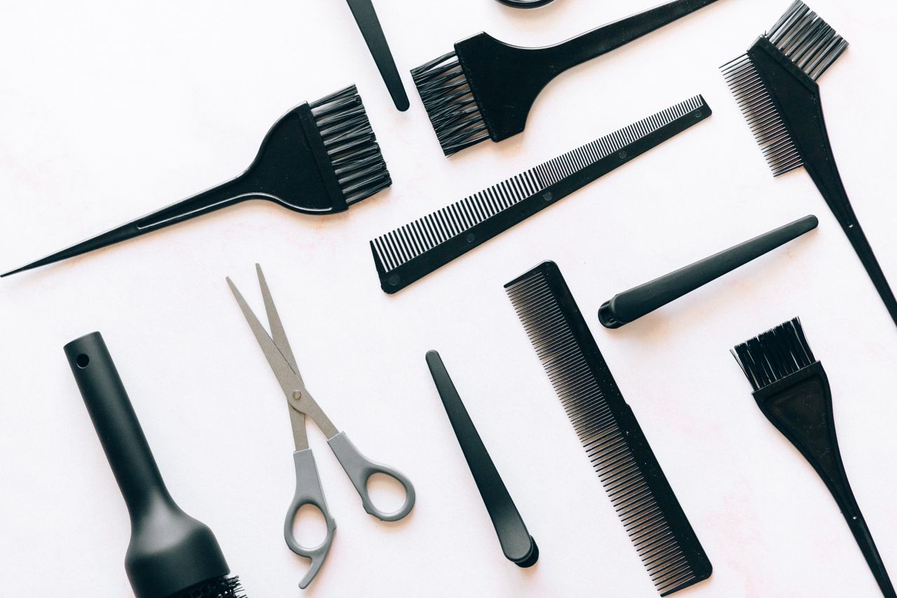 Strona Główna Flat lay of essential hairdressing tools including brushes, combs, and scissors on white background.